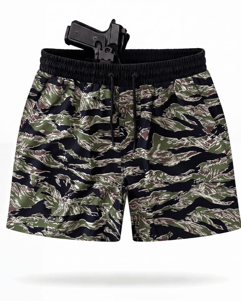 A pair of men's tiger stripe camouflage shorts in green, brown, and black, featuring a black elastic waistband and drawstring, shown with a black holster containing a handgun on a white background.