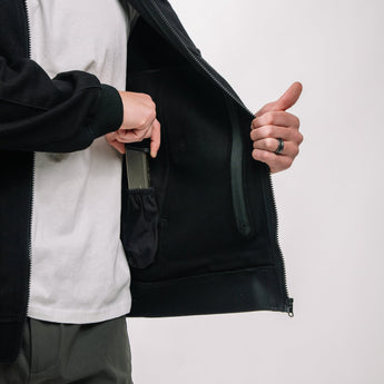 Person opening a black jacket with a white interior on a light gray background