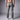 Rear view of a man wearing crater grey chinos with a brown leather belt and white sneakers, against a gray studio background.