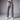 A man wearing crater grey chinos without a belt, using the drawstring waistband to carry a black holstered handgun, with white sneakers against a gray studio background.