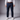 A man wearing navy blue chinos, a brown leather belt, a white long-sleeve button-up shirt tucked in, and white sneakers, shown from the waist down against a gray studio background.